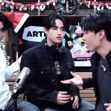 two men are talking in front of a sign that says arti on it