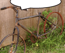 an old rusty bicycle is leaning against a wooden fence and has a speech bubble above it