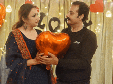 a man and a woman are holding a heart shaped balloon in front of a sign that says love