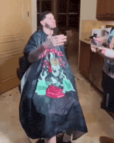a man is getting his hair cut by a man wearing a black cape with a skull on it