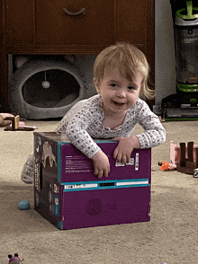 a little girl is playing with a purple box that has a sticker that says ' snoopy ' on it