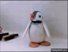 a stuffed penguin with a pink nose is standing on a table .