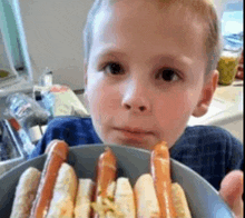 a young boy is holding a bowl of hot dogs in his hands .