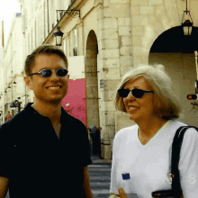 a man and a woman are walking down a street and the man is wearing sunglasses