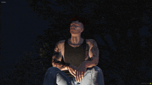 a man in a black tank top sits under a tree at night