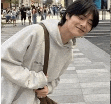 a young man wearing a hoodie is standing on a sidewalk holding a bag .