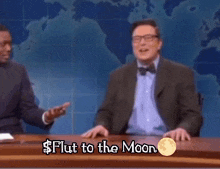 a man in a suit and bow tie is talking to another man in front of a map of the world and the words $ flut to the moon