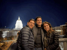 three people posing for a picture in front of a building that says capitol