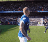 a man in a blue shirt is running on a soccer field in front of a sign that says umbro