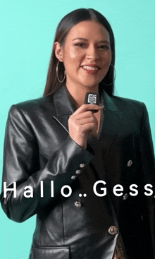 a woman in a black leather jacket is holding a microphone with the words hallo gess written on it