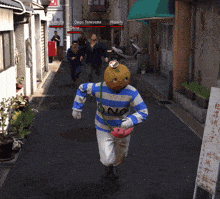 a man in a blue and white striped sweater with a pumpkin on his head is running down a street