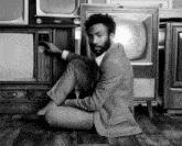 a man in a suit is sitting in front of a stack of old televisions including one that says u.s. army