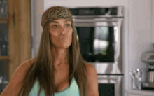 a woman wearing a bandana is standing in a kitchen .