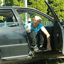 a man in a blue shirt is sitting in a car holding a bottle of water