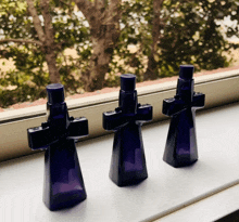 three small blue bottles in the shape of crosses are sitting on a window sill