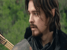 a man with long hair and a beard is holding an arrow in his hand .