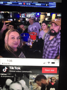 a screen shows a group of people standing around a table with a tiktok app open on the bottom