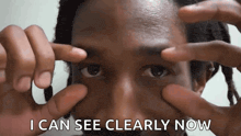 a man with dreadlocks is covering his eyes with his hands and the words i can see clearly now are above him .