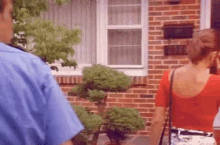 a man in a blue shirt is talking to a woman in a red top in front of a brick house with the address 2098