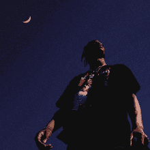 a man in a black shirt with a skeleton on it is looking up at a crescent moon