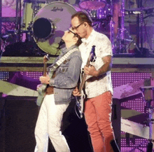 a man and a woman playing guitars on a stage with a ludwig drum behind them