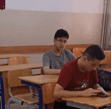 two boys are sitting at desks in a classroom with a laptop .