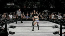 two women are wrestling in a ring with a referee in the background