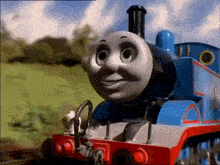 thomas the train is smiling and looking at the camera while standing on the tracks .