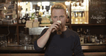 a man drinking a glass of beer in front of a bar with a sign that says ' hauswein ' on it