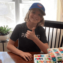 a young boy giving a thumbs up while wearing a blue hat