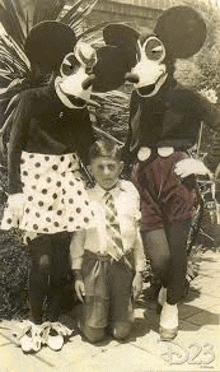 a black and white photo of mickey mouse and minnie mouse standing next to a boy .