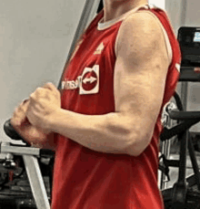 a man in a red tank top is standing in a gym and flexing his muscles .