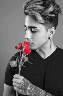 a man with a tattoo on his arm is holding a red rose in his hand .