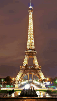 the eiffel tower is lit up at night with a fountain in front of it