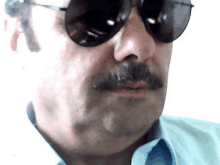 a man with a mustache wearing sunglasses and a light blue shirt