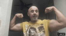 a man in a yellow shirt is flexing his muscles in front of a ceiling fan