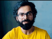 a man with a beard and glasses is wearing a yellow shirt and looking at the camera .