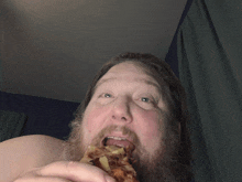 a shirtless man with a beard is eating a pizza