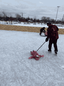 a little girl is laying on the ice being pulled by a man wearing a jacket that says ' slazen '