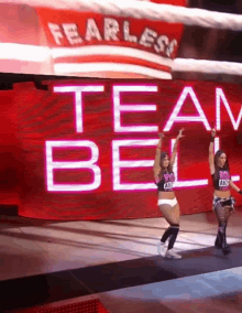 two female wrestlers are standing in front of a large screen that says team bell