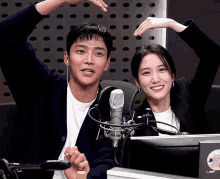 a man and a woman making a heart shape with their hands in front of a microphone