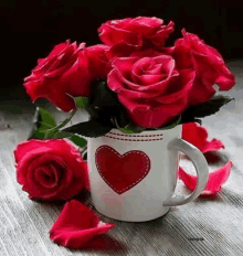 a cup filled with red roses and petals on a table .