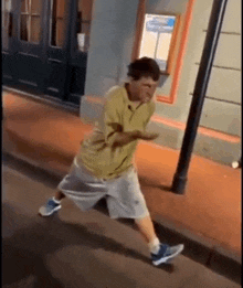 a man in a yellow shirt and grey shorts is running down a sidewalk .