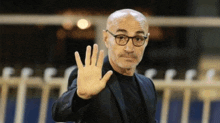 a bald man wearing glasses and a suit is making a stop gesture with his hand