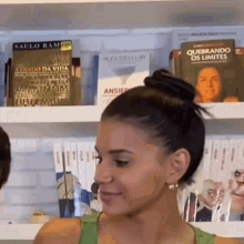 a woman in a green tank top stands in front of a shelf with books on it including one titled quebrando os limites