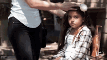 a woman is putting a headband on a little girl 's head with the letter c on the bottom right