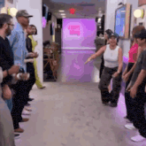 a woman is dancing in front of a group of people in a hallway with a purple wall that says jumping bunny