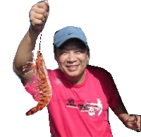 a man in a pink shirt is holding a shrimp in his hand