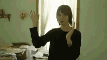 a woman in a black shirt is standing in front of a window and waving her hand .