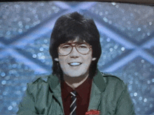 a man with glasses and a green jacket is smiling on a television screen